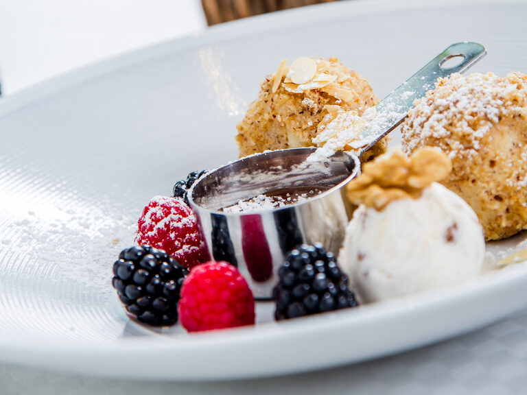 Auf einem weißen Teller ist Eis mit Beeren und kleinen Kuchen angerichtet