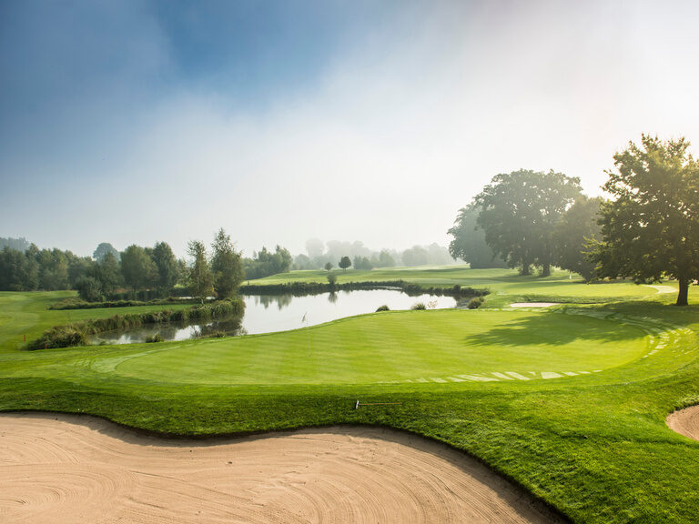 Natur & Golf Ein Sportgelände mit einem Teich und Bäumen im Hintergrund